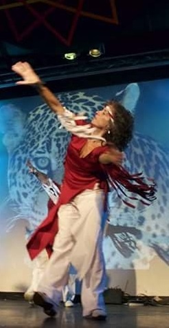 A female dancer in motion on an indoor stage wearing a maroon and white costume.